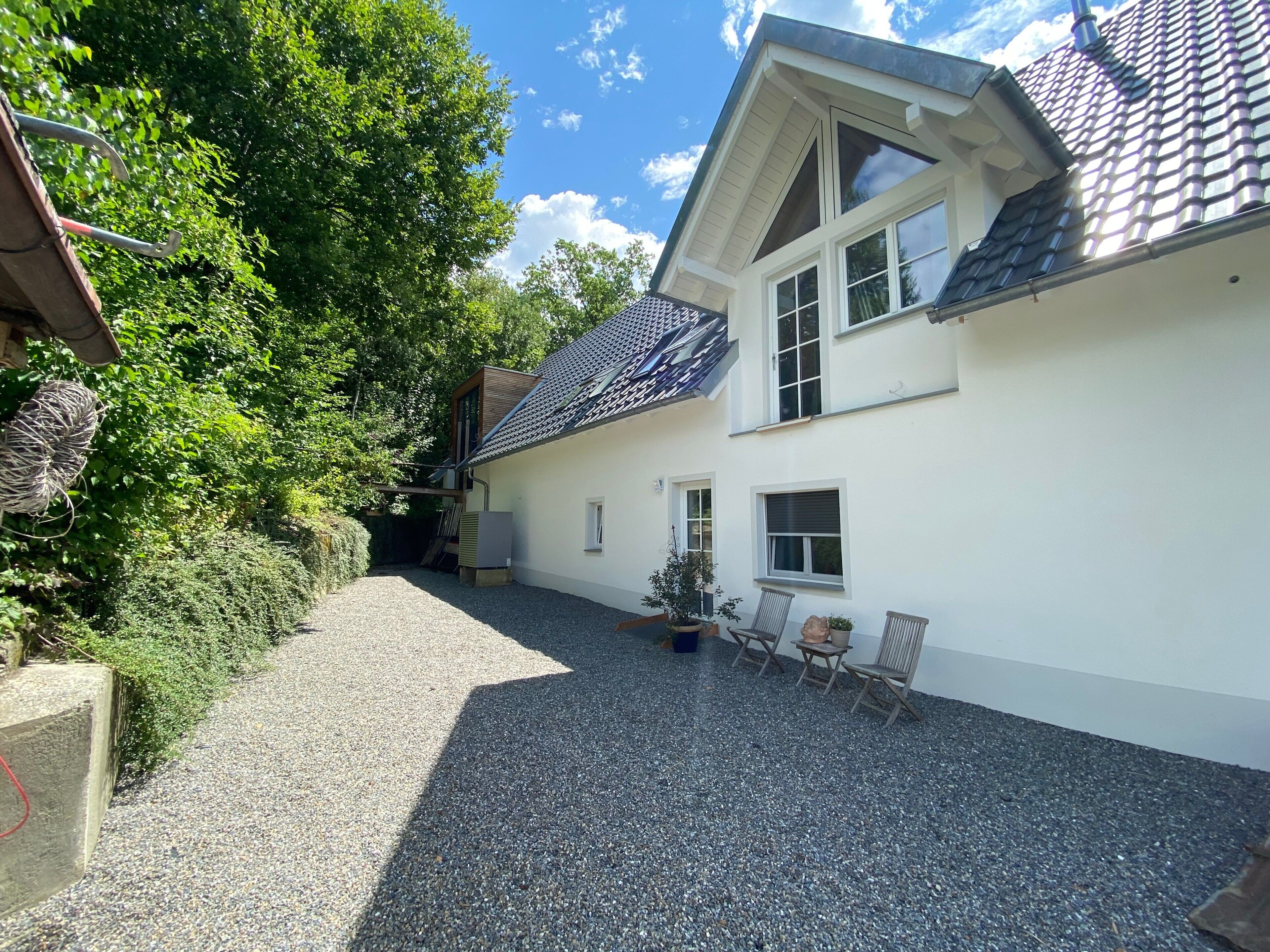 Ein Haus mit Kiesweg, einer überdachten Terrasse mit Sitzgelegenheiten und einem Garten.
