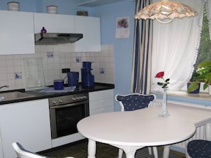 A kitchen with white cabinets, a stove, and blue kitchenware. There is a table with a vase of a single red rose.