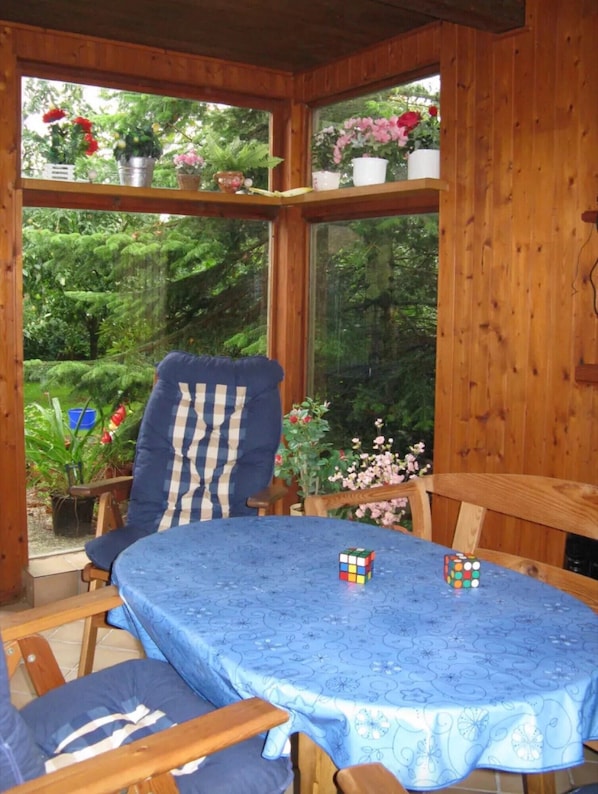 A wooden-paneled room with a table and chairs, a window with plants, and a view of greenery.
