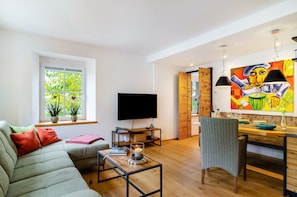 Un salon moderne avec un canapé, un téléviseur, un coin repas et un tableau accroché au mur.