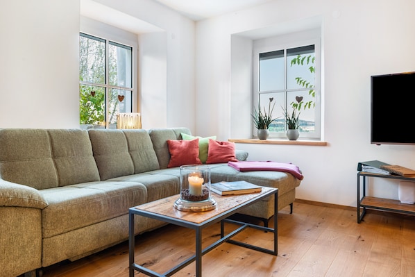 Un salon avec un canapé, une table basse sur laquelle est posée une bougie, et un téléviseur fixé au mur.
