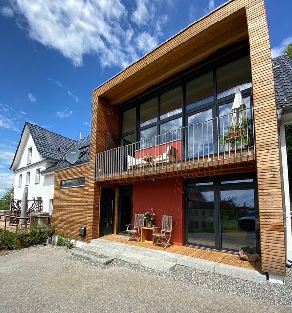 A modern two-story building with a balcony, large windows, and a red facade.