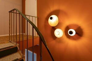 A staircase with a metal railing, wooden steps, and a wall with three wall-mounted light fixtures.