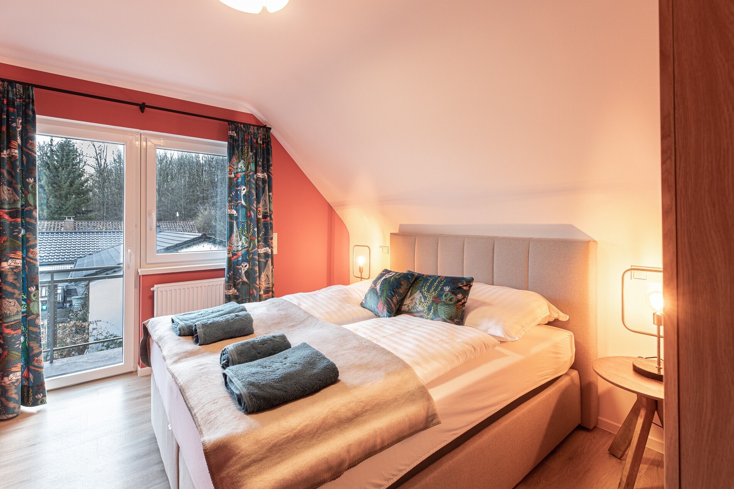 Ein Schlafzimmer mit einem großen Bett, Blick durch eine Schiebetür und einem Nachttisch mit Lampe.