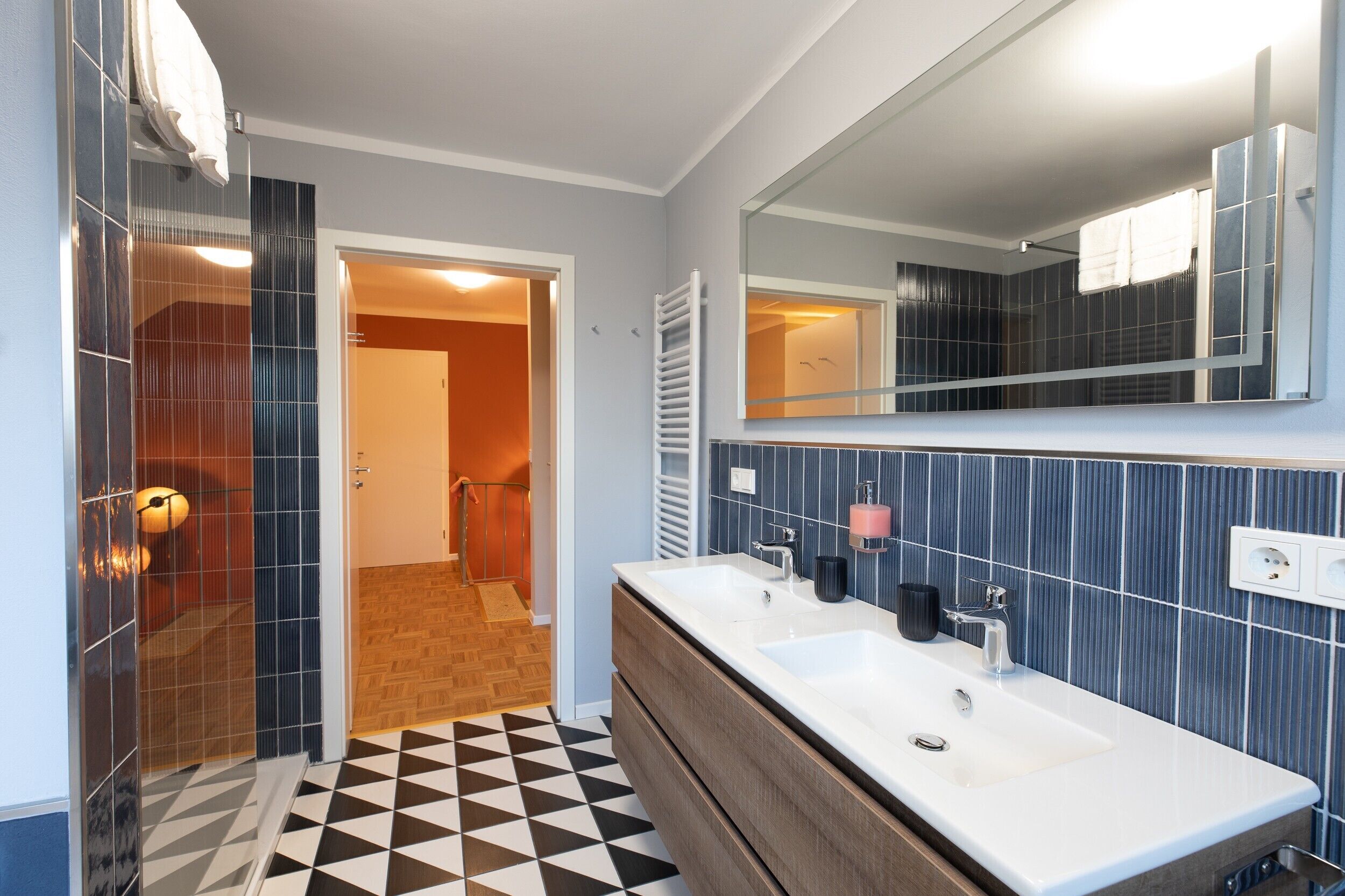Un bagno con doppio lavandino, uno specchio e pavimento piastrellato.