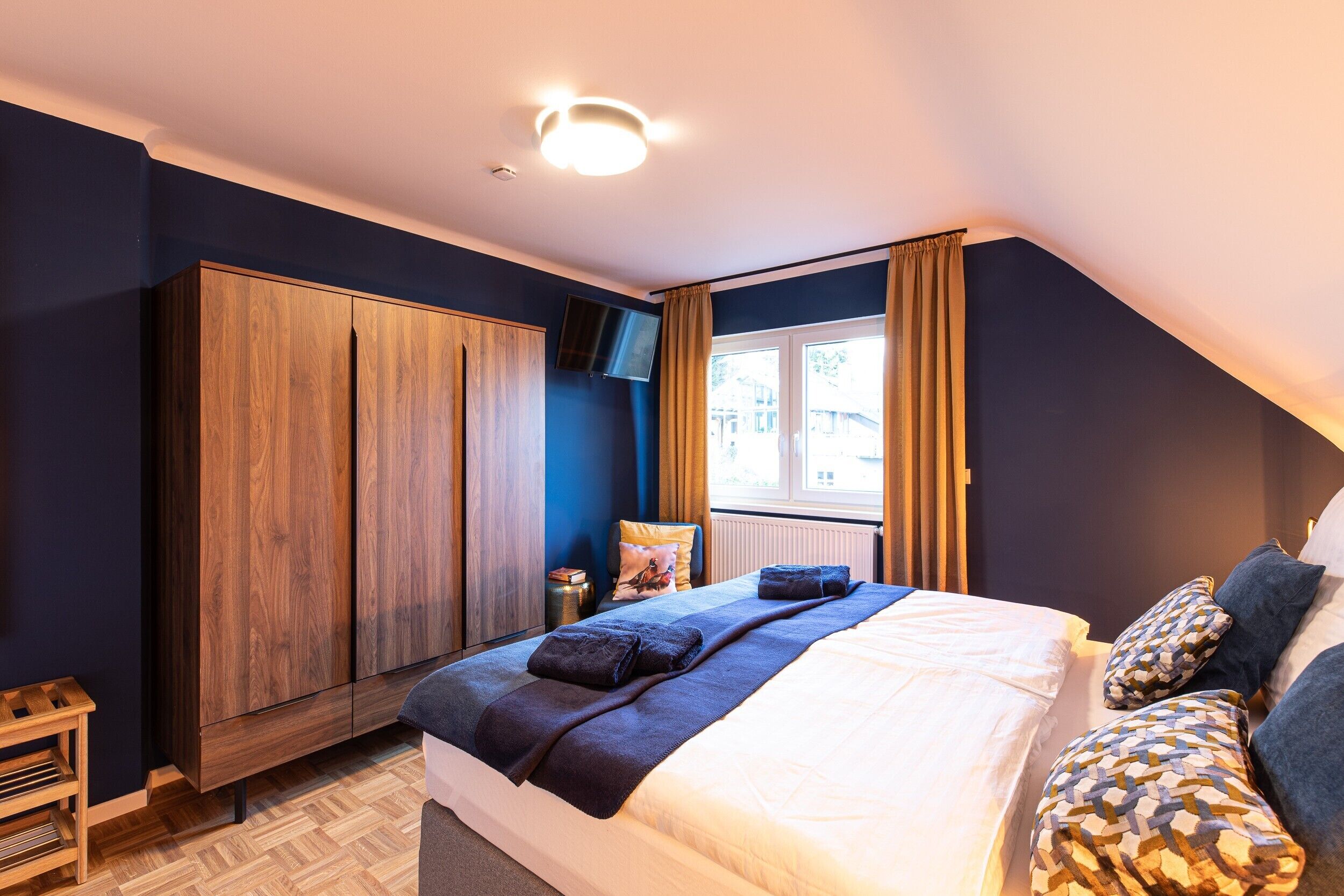 A bedroom with a bed, a wardrobe, a TV, and a window with curtains.