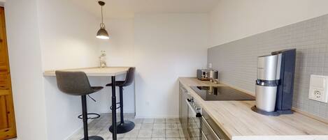A compact kitchen with a dining area, a coffee machine, and a small refrigerator.