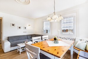 Un espace de vie compact comprenant une table à manger en bois, des chaises blanches, un canapé gris et un divan blanc.
