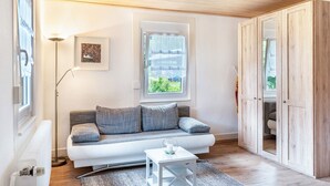 Sala de estar moderna com sofá branco, luminária de chão, uma mesinha e vista pela janela.