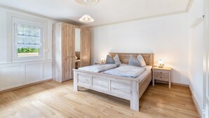 Quarto com cama de madeira, mesas de cabeceira, uma janela e luminária no teto.