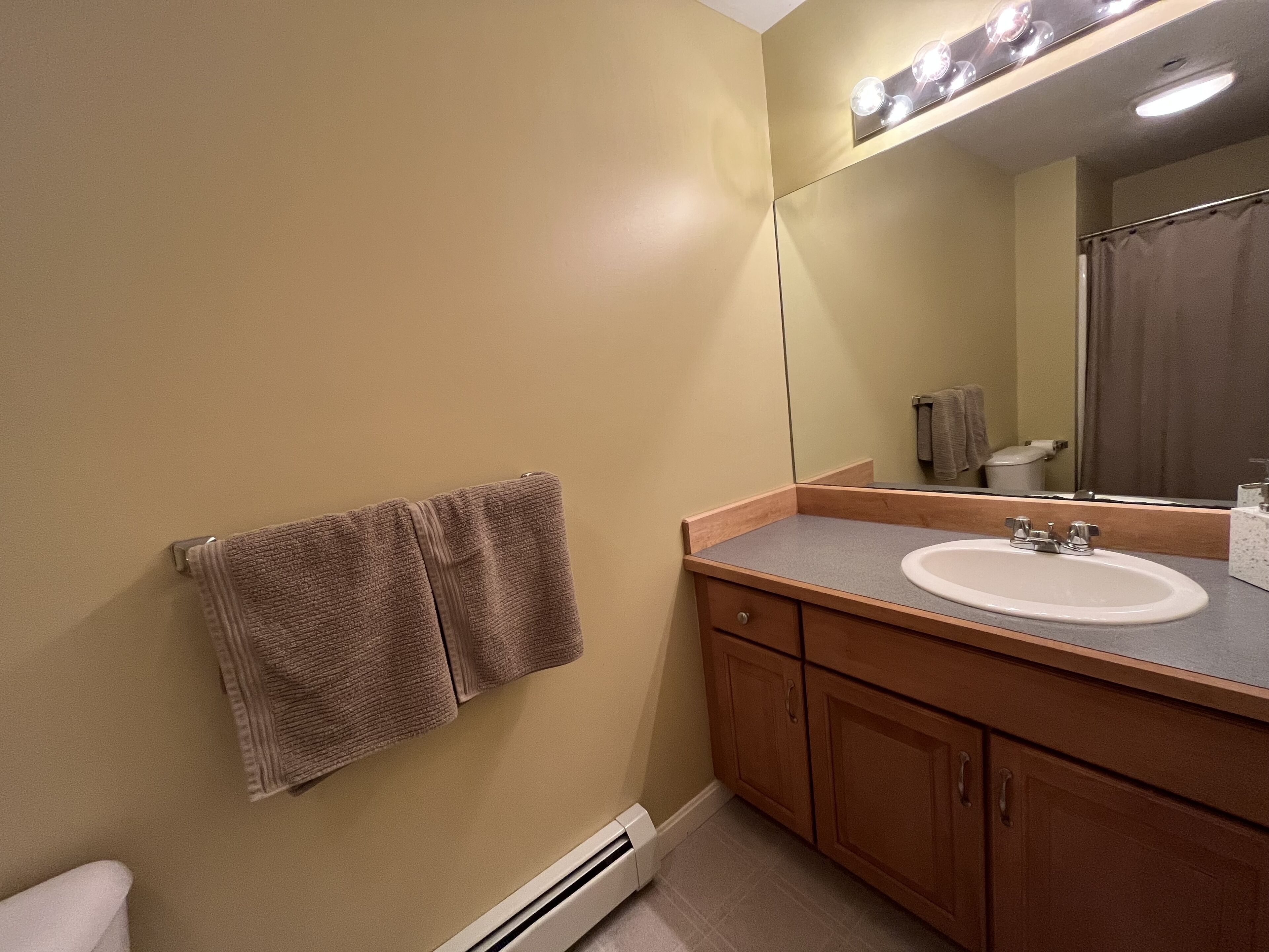 Un baño con pared color beige, un mueble de tocador de madera con lavamanos y un perchero para toallas.