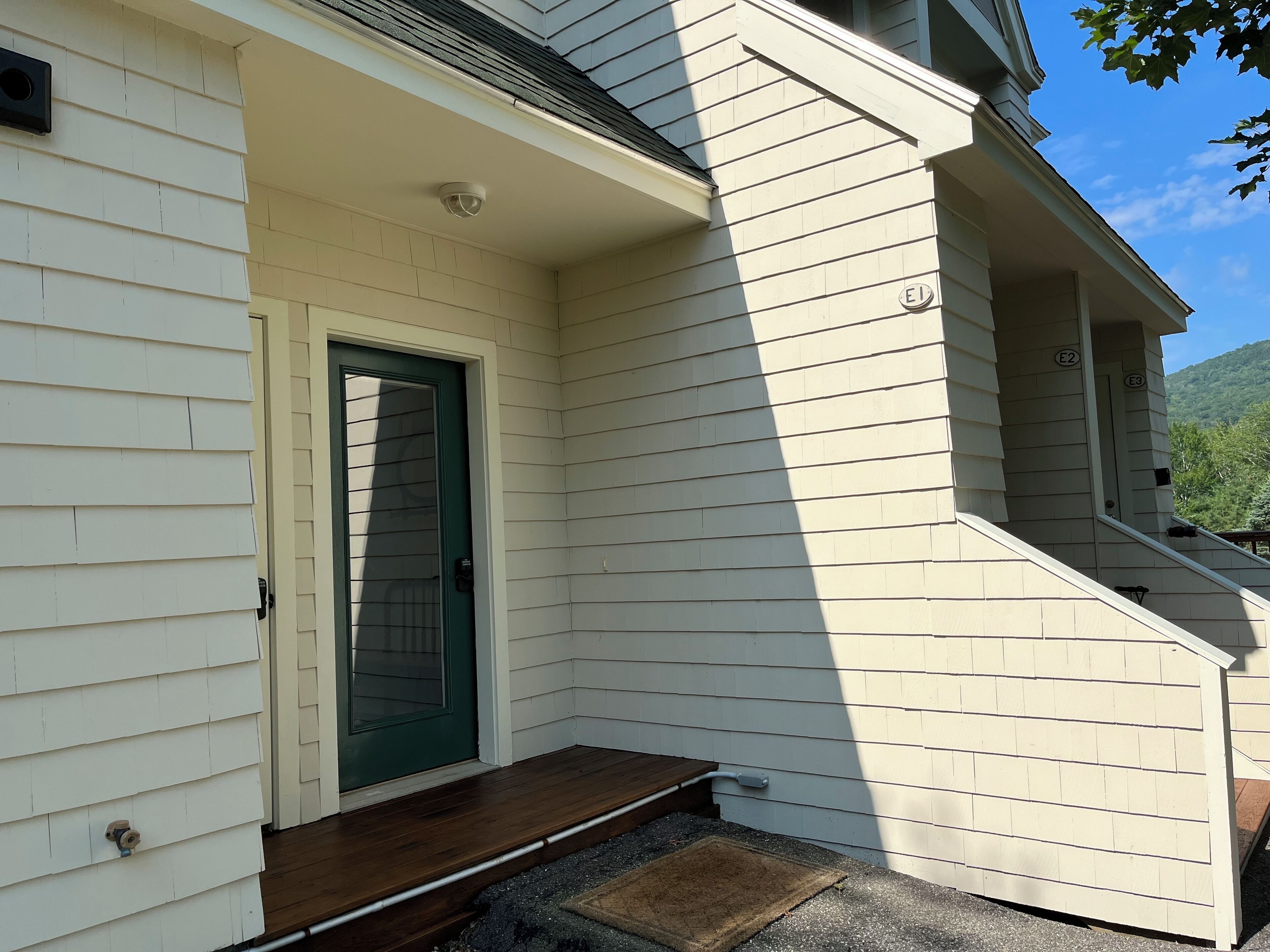 Une maison avec une porte verte, un petit porche et un escalier menant à l’étage supérieur.