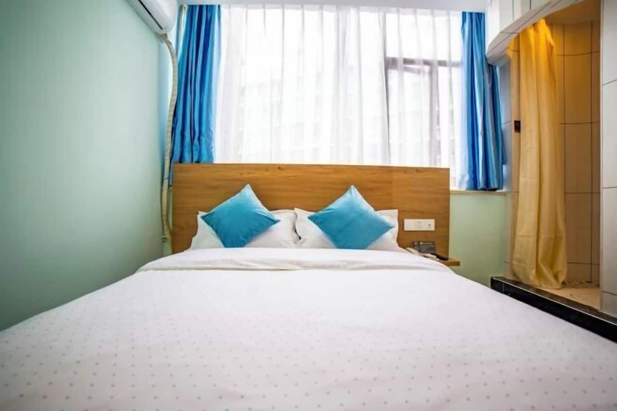 A bed with a wooden headboard, two blue pillows, and a white bedspread with small patterns.