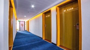 Pasillo de hotel con alfombra azul, puertas de madera con números de habitación e iluminación empotrada en el techo.