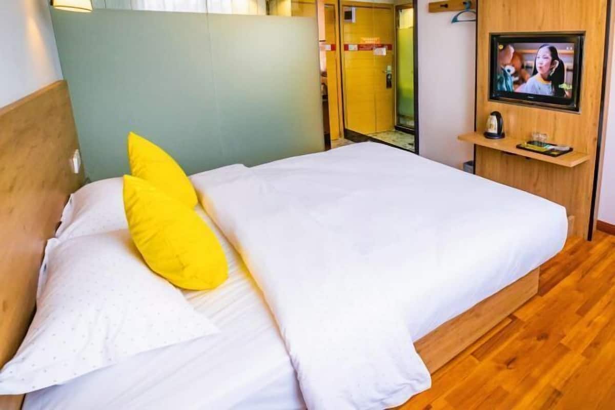 A hotel room with a bed, a television, and a wooden floor.