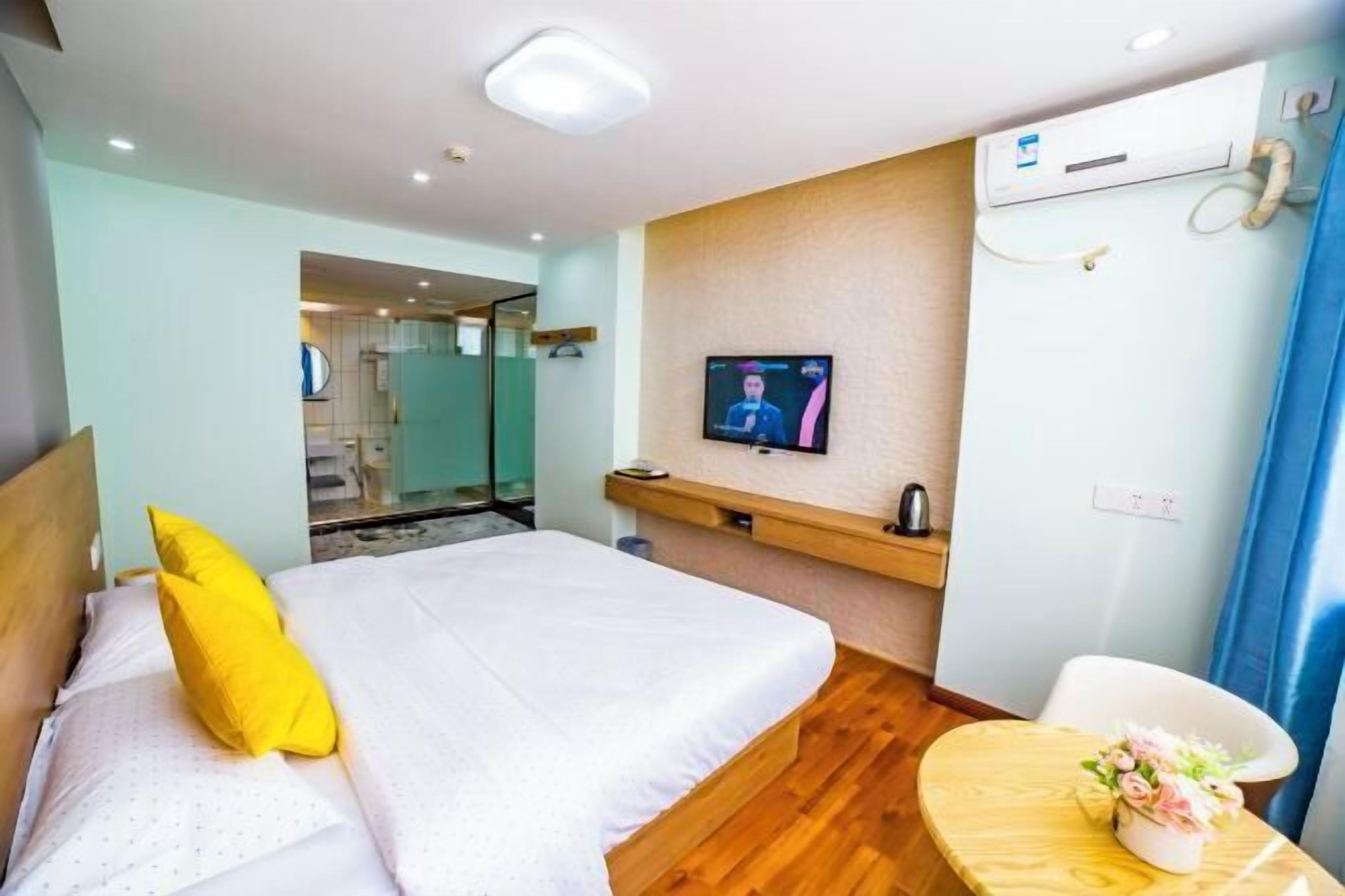 Habitación de hotel con cama, televisión, una mesita con un florero y un aire acondicionado instalado en la pared.