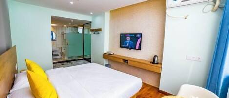 Habitación de hotel con cama, televisión, una mesita con un florero y un aire acondicionado instalado en la pared.