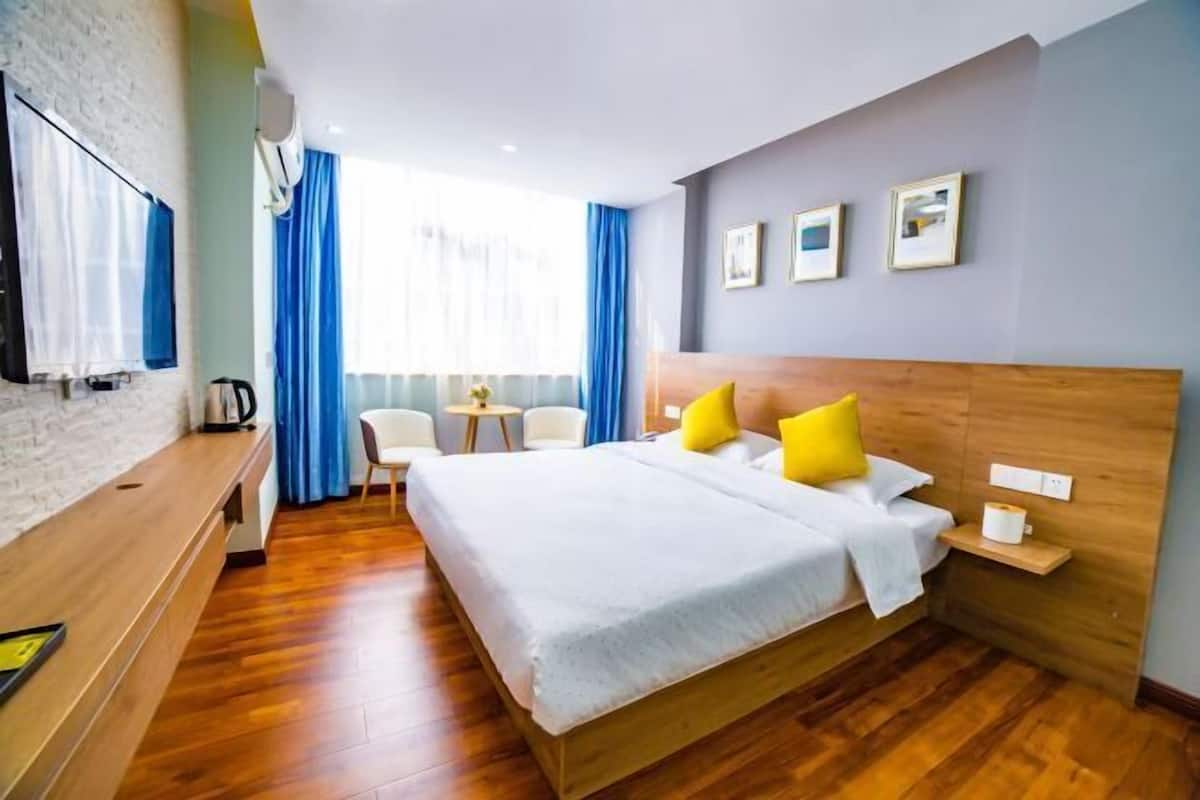 A hotel room with a wooden bed, a desk, a chair, a TV, and a window with curtains.