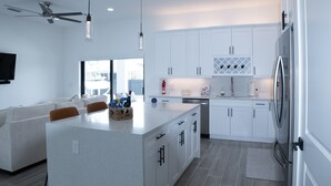 A modern kitchen with white cabinetry, a central island, and a dining area with a sofa and chairs. - Welcome to Corallo house - Heated Pool - Pet friendly - Relaxing Gateway  (Cape Coral)