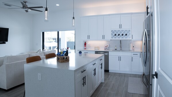 A modern kitchen with white cabinetry, a central island, and a dining area with a sofa and chairs.