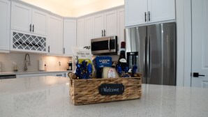 A kitchen with white cabinets, a stainless steel refrigerator, a microwave, and a wicker basket with a 'Welcome' sign on a marble countertop. - Welcome to Corallo house - Heated Pool - Pet friendly - Relaxing Gateway  (Cape Coral)