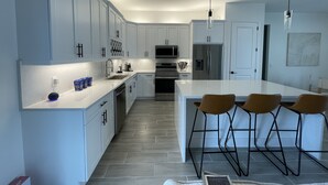 A modern kitchen with white cabinetry, a central island with bar stools, stainless steel appliances, and pendant lighting. - Welcome to Corallo house - Heated Pool - Pet friendly - Relaxing Gateway  (Cape Coral)