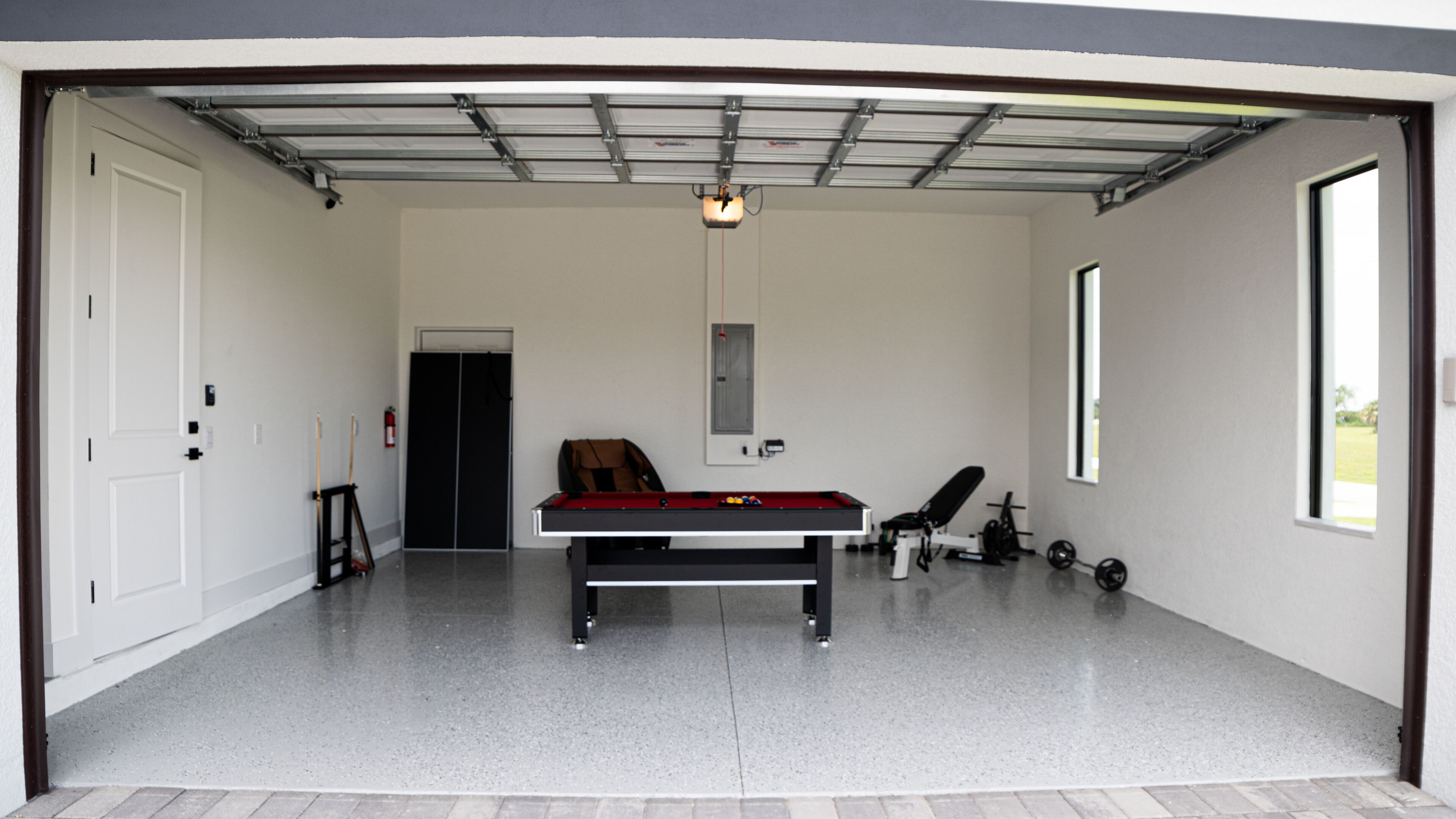 Un grand garage comprenant une table de billard, du matériel de musculation et une porte donnant sur une autre pièce.
