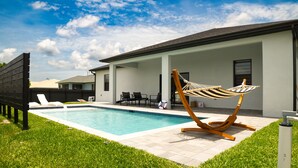 A modern outdoor pool area with a hammock, lounge chairs, and a covered patio. - Welcome to Corallo house - Heated Pool - Pet friendly - Relaxing Gateway  (Cape Coral)