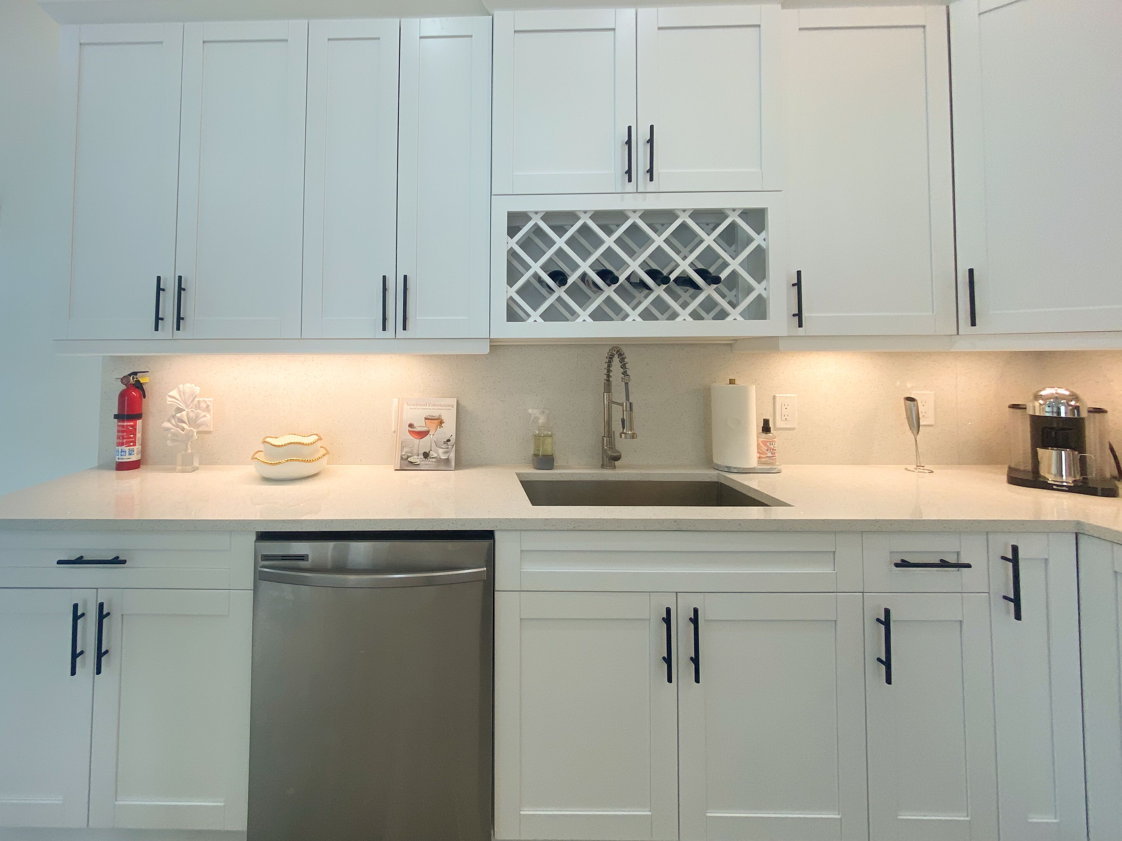 Een moderne keuken met witte kasten, een roestvrijstalen vaatwasser en een geïntegreerde wijnkoeler.