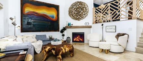 A modern living room with a fireplace, a large abstract painting, and a wooden staircase.
