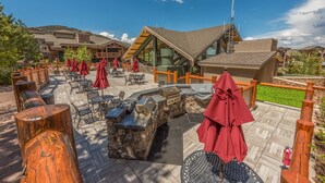 An outdoor patio area with stone tables, red umbrellas, and a grill station. - Westgate 1BR, private balcony, resort amenities, multiple pools, tennis, onsite spa, restaurant (Park City)