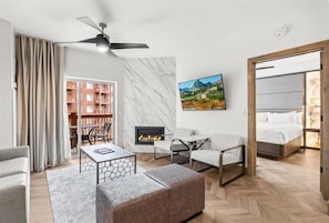 A modern hotel room with a fireplace, a sofa, a coffee table, and a view of a mountain landscape.