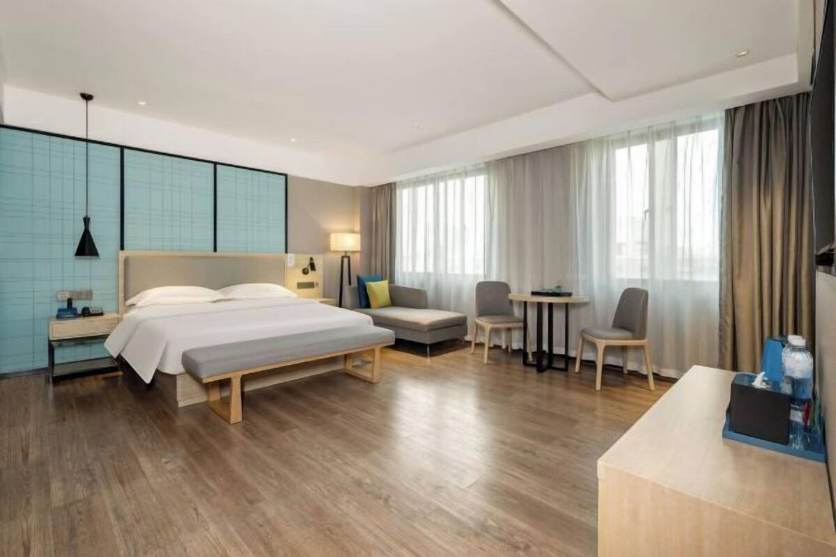 A modern hotel room with a large bed, a desk, a chair, and a small table.