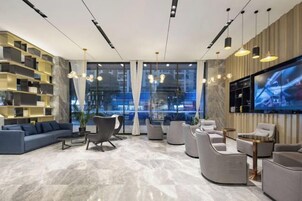 A modern lobby with a sofa, armchairs, a TV, and a bookshelf.