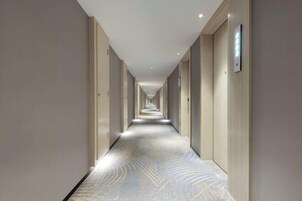 Un pasillo largo y estrecho en un hotel, con suelo estampado y puertas a ambos lados.