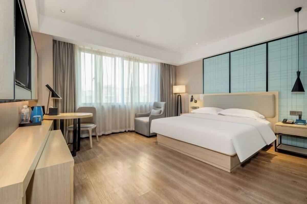 A modern hotel room with a large bed, a desk, a chair, and a small table.
