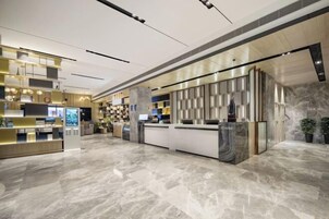 A modern hotel lobby with a marble floor, a reception desk, and a digital information kiosk.