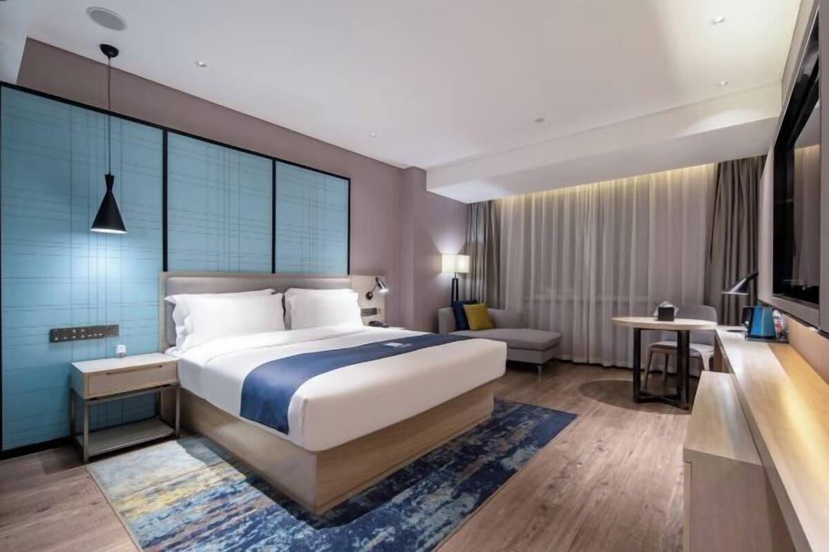 A modern hotel room with a large bed, bedside tables, a desk, and a TV.