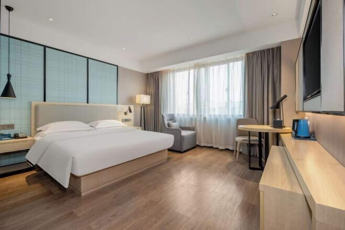 A modern hotel room with a large bed, a desk, a chair, and a TV.