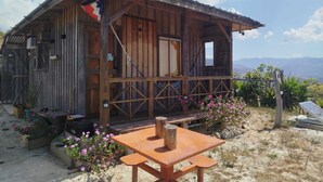 Un chalet rustique en bois doté d’un balcon, entouré de plantes en fleurs et offrant une vue dégagée sur les montagnes.