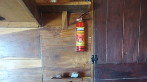 Un intérieur en bois, avec une porte en bois foncé, une étagère sur laquelle se trouve un extincteur, et une petite table agrémentée d’un objet décoratif.