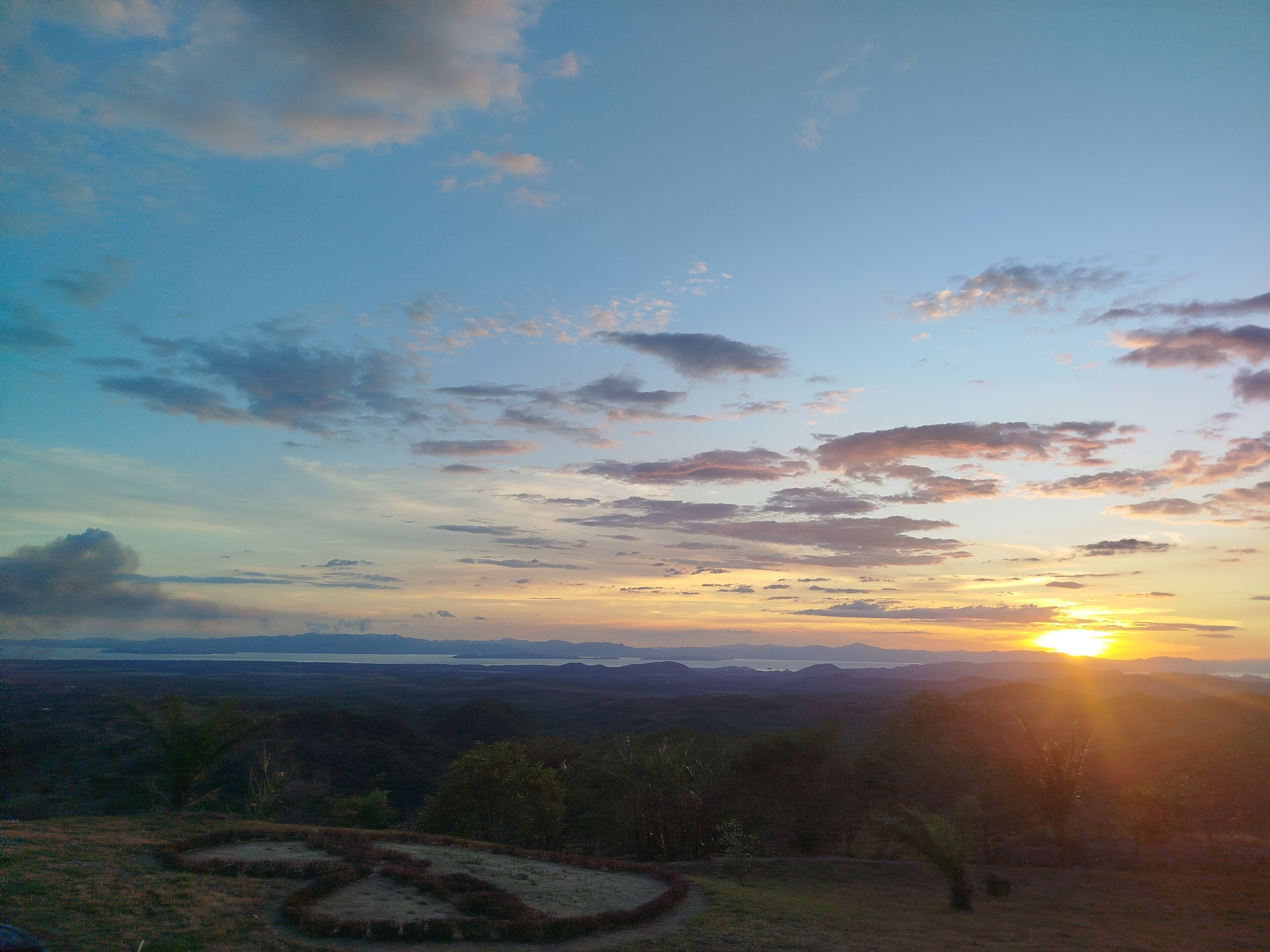 A landscape with a sunset, hills, and a clear sky.