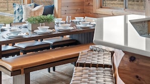 Een houten chalet van binnen, met een eethoek, grote ramen en een hanglamp.