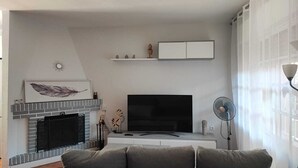 A modern living room with a fireplace, a flat-screen TV, a sofa, and a fan.