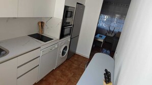 A compact kitchen with white cabinets, a built-in oven, a microwave, and a washing machine.
