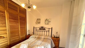 A bedroom with a bed, wooden wardrobe, bedside tables, and a chandelier.