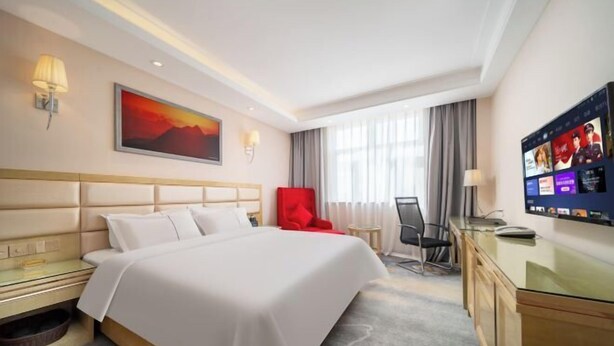 A hotel room with a bed, a desk, a TV, a chair, and a painting on the wall. - Boyu Hotel (Karamay)