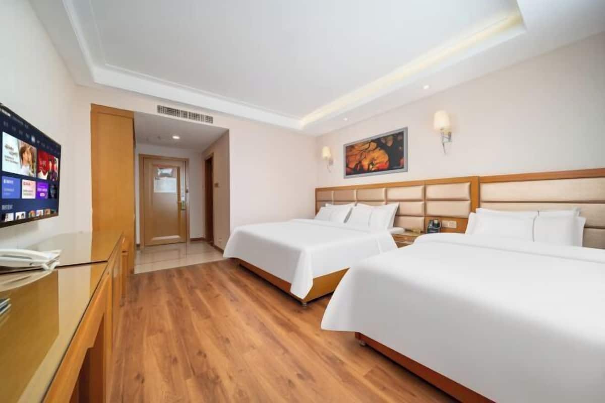 Una habitación de hotel con dos camas, un escritorio, un televisor y un cuadro en la pared.