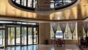 Eine Hotelhalle mit einem großen Kronleuchter, einem Empfangsbereich und Blick ins Freie durch große Fenster.