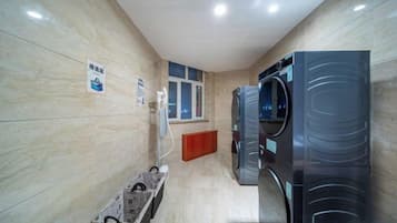 A laundry facility with two large washing machines, a drying machine, and a small trash bin.